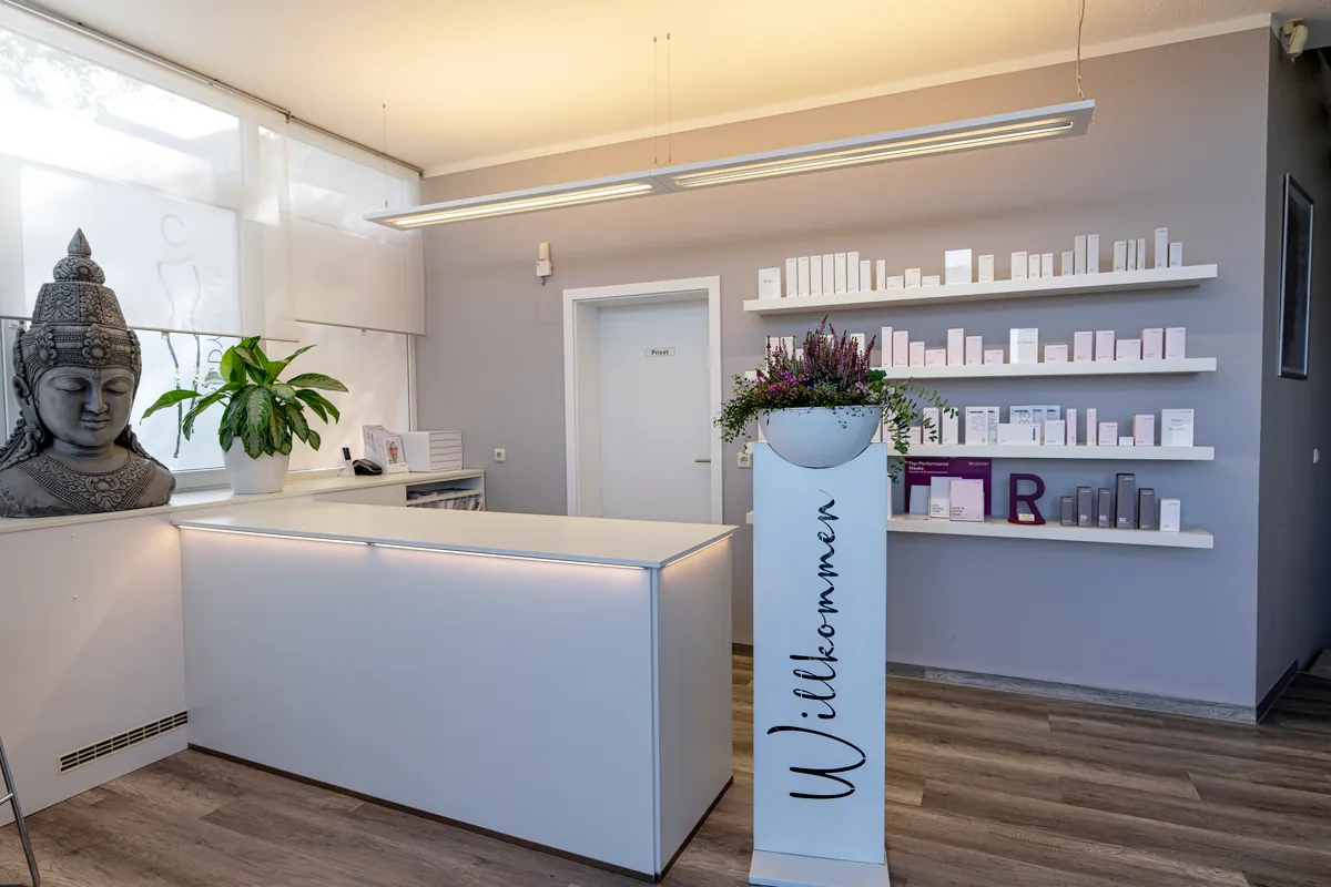 Empfangstheke mit Pflegeprodukten und Willkommen-Aufsteller bei BodyFlair Werdau