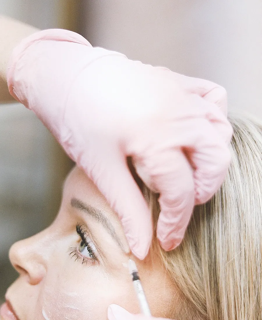 Injektion an der Wange einer Kundin mit rosa Handschuhen